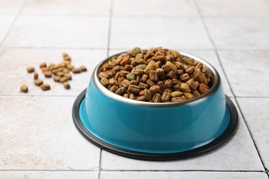 Photo of Dry pet food in feeding bowl on light tiled background, closeup