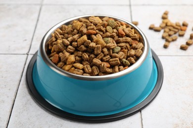 Photo of Dry pet food in feeding bowl on light tiled background, closeup