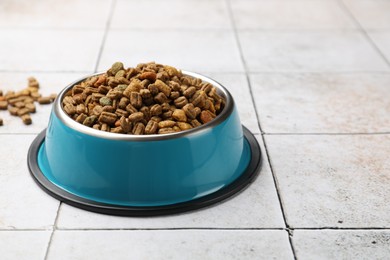 Photo of Dry pet food in feeding bowl on light tiled background, closeup