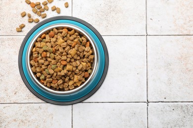 Photo of Dry pet food in feeding bowl on light tiled background, top view. Space for text