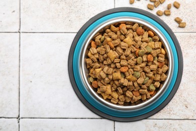 Photo of Dry pet food in feeding bowl on light tiled background, top view. Space for text