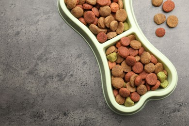 Photo of Dry pet food in feeding bowl on gray textured background, top view. Space for text