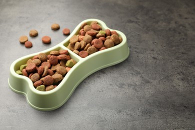 Photo of Dry pet food in feeding bowl on gray textured background, closeup. Space for text