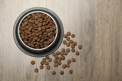 Photo of Dry pet food in feeding bowl on wooden background, top view. Space for text