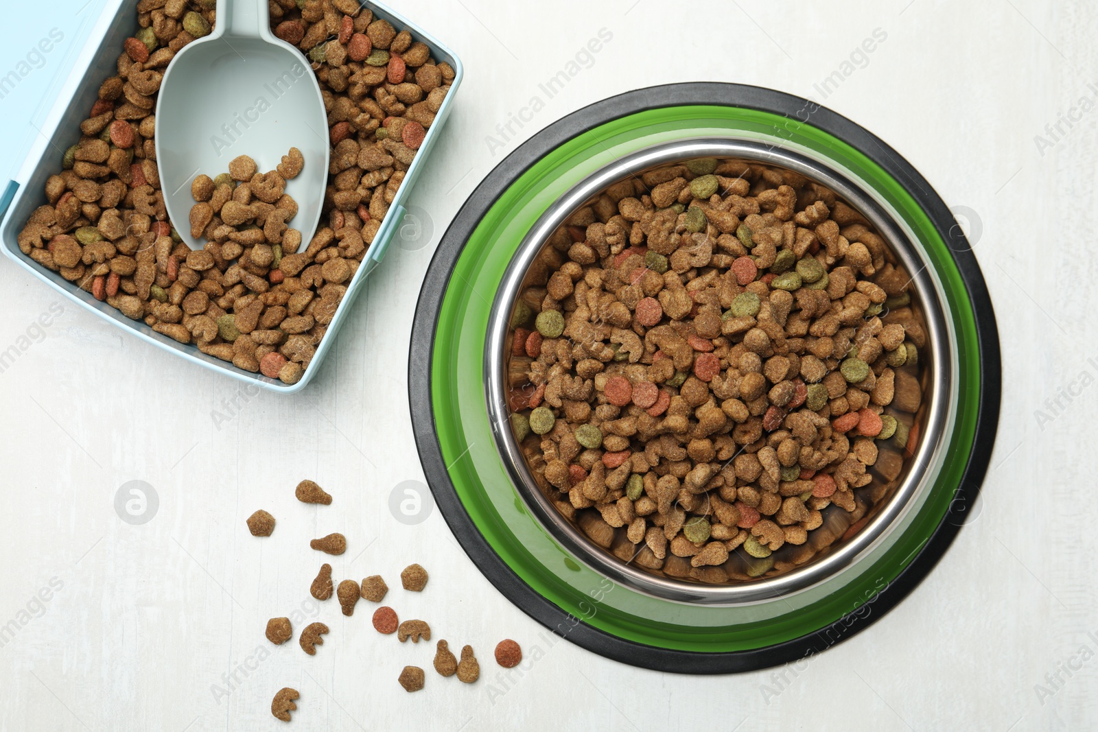 Dry pet food in feeding bowl, container and scoop on light background, flat lay Photo of Dry pet food in feeding bowl, container and scoop on light background, flat lay