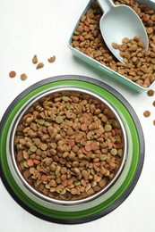 Photo of Dry pet food in feeding bowl, container and scoop on light background, flat lay