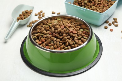 Photo of Dry pet food in feeding bowl, container and scoop on light background, closeup