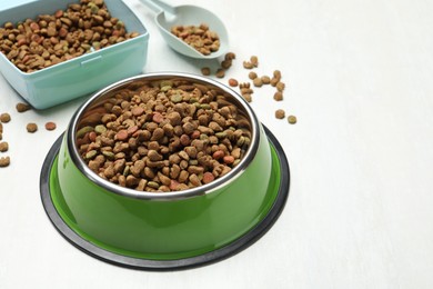 Photo of Dry pet food in feeding bowl, container and scoop on light background, closeup