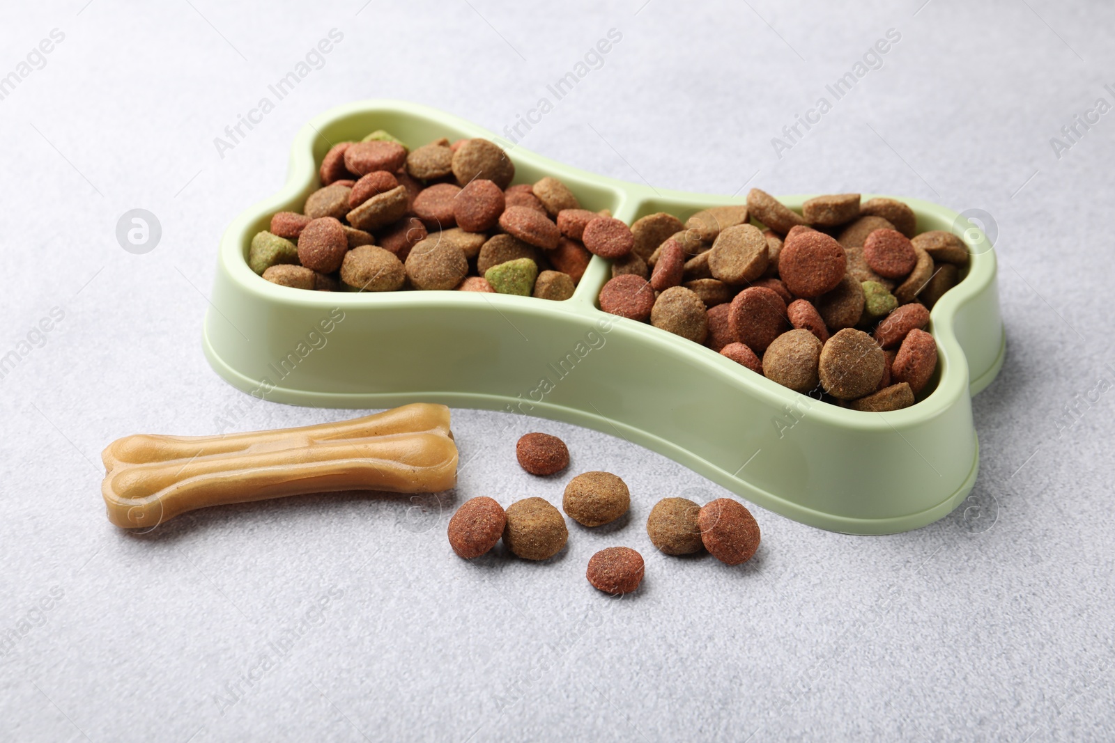 Dry pet food in feeding bowl and chew bone on gray background, closeup Photo of Dry pet food in feeding bowl and chew bone on gray background, closeup