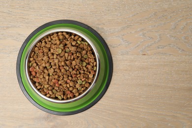 Photo of Dry pet food in feeding bowl on wooden background, top view. Space for text
