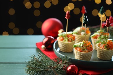 Photo of Tasty canapes and Christmas decor on green wooden table against black background with blurred lights, space for text. Bokeh effect