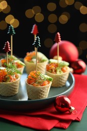 Photo of Tasty canapes and Christmas decor on table against black background with blurred lights, closeup. Bokeh effect