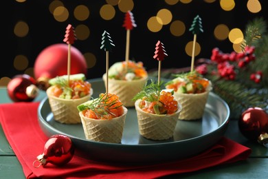Photo of Tasty canapes and Christmas decor on green wooden table against black background with blurred lights, closeup. Bokeh effect