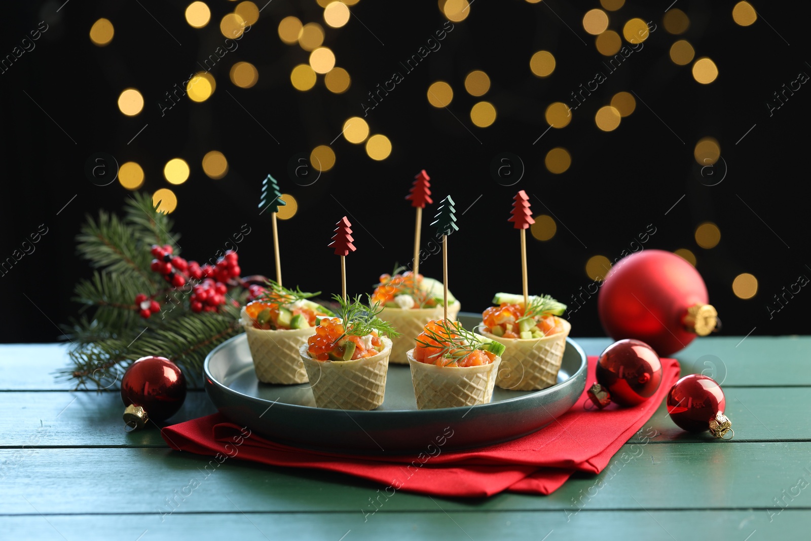 Tasty canapes and Christmas decor on green wooden table against black background with blurred lights Photo of Tasty canapes and Christmas decor on green wooden table against black background with blurred lights