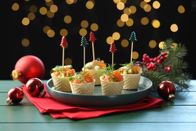 Photo of Tasty canapes and Christmas decor on green wooden table against black background with blurred lights