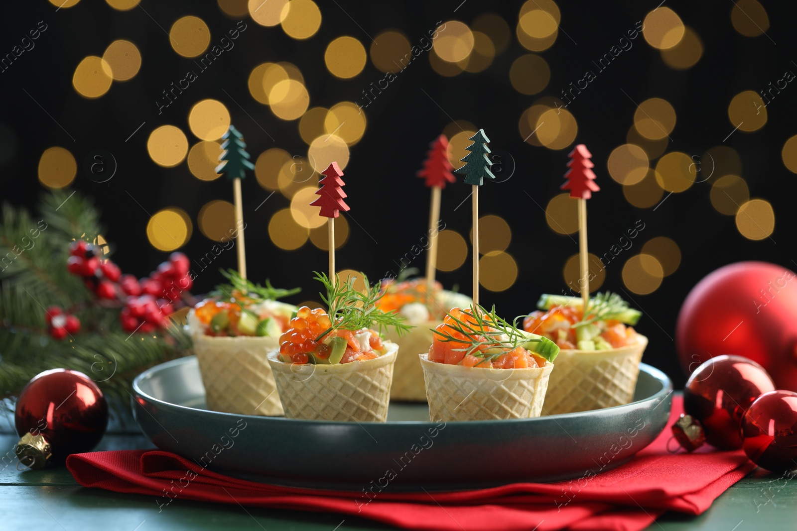 Photo of Tasty canapes and Christmas decor on green wooden table against black background with blurred lights, closeup. Bokeh effect