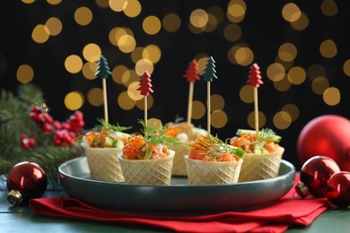 Photo of Tasty canapes and Christmas decor on green wooden table against black background with blurred lights, closeup. Bokeh effect