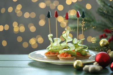 Photo of Tasty canapes and Christmas decor on green wooden table against background with blurred lights, space for text. Bokeh effect