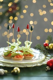 Photo of Tasty canapes and Christmas decor on green wooden table against background with blurred lights, closeup. Bokeh effect