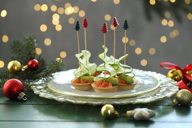 Photo of Tasty canapes and Christmas decor on green wooden table against background with blurred lights, closeup. Bokeh effect