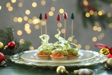 Photo of Tasty canapes and Christmas decor on green wooden table against background with blurred lights, closeup. Bokeh effect