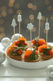 Photo of Tasty canapes and Christmas decor on white wooden table against background with blurred lights, closeup. Bokeh effect