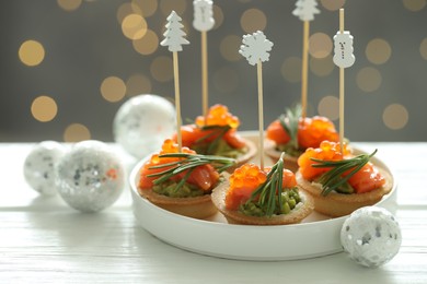 Photo of Tasty canapes and Christmas decor on white wooden table against background with blurred lights, closeup. Bokeh effect