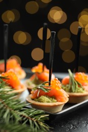 Photo of Tasty canapes and Christmas decor on black table against dark background with blurred lights, closeup. Bokeh effect