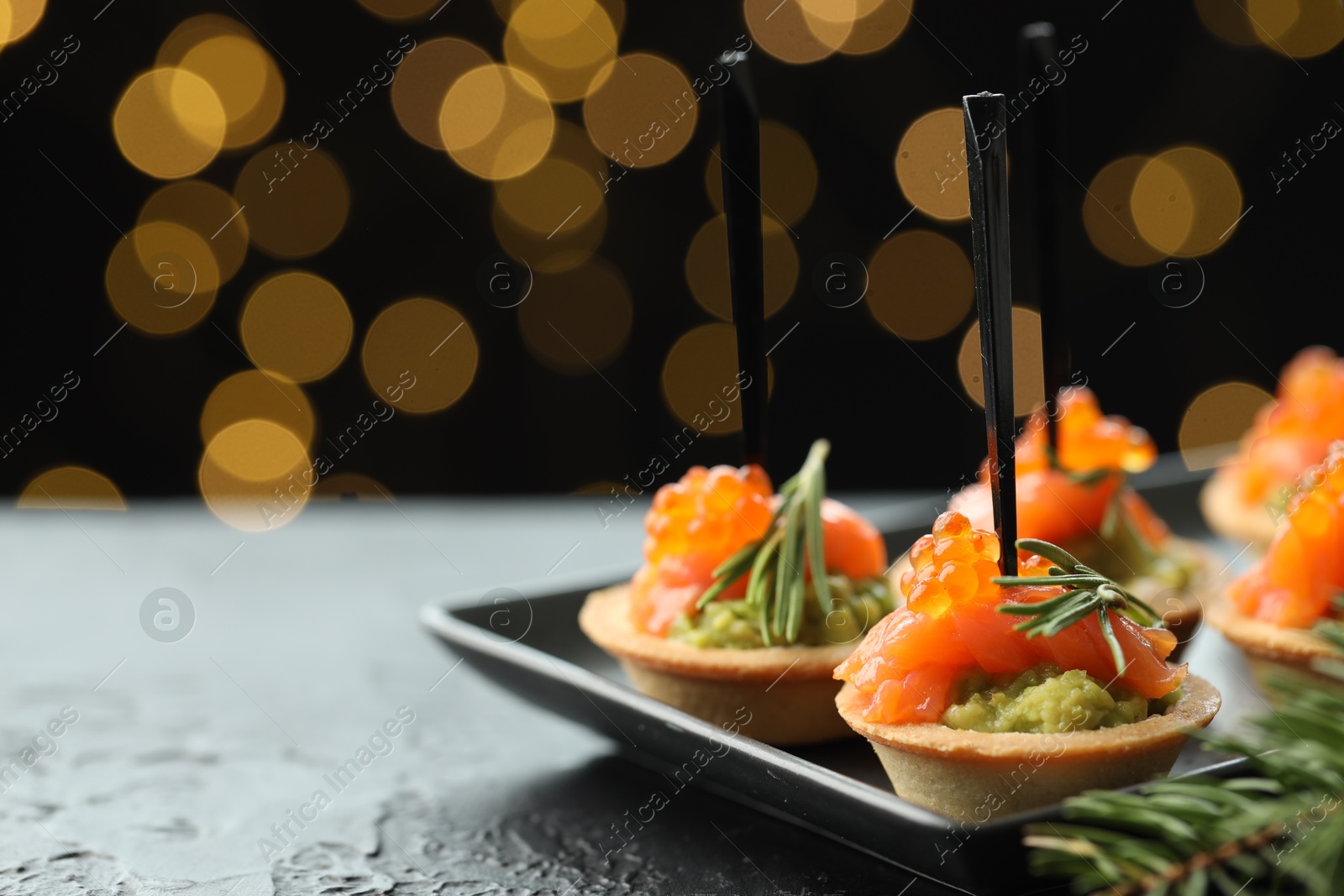 Photo of Tasty canapes and Christmas decor on black table against dark background with blurred lights, space for text. Bokeh effect