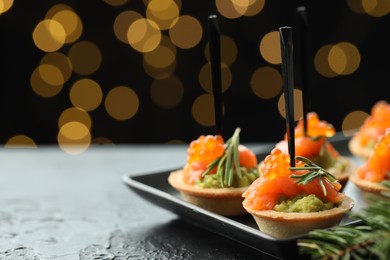 Photo of Tasty canapes and Christmas decor on black table against dark background with blurred lights, space for text. Bokeh effect