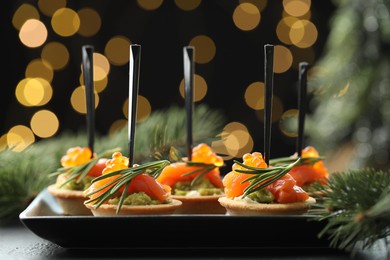 Photo of Tasty canapes and Christmas decor on table against dark background with blurred lights, closeup. Bokeh effect