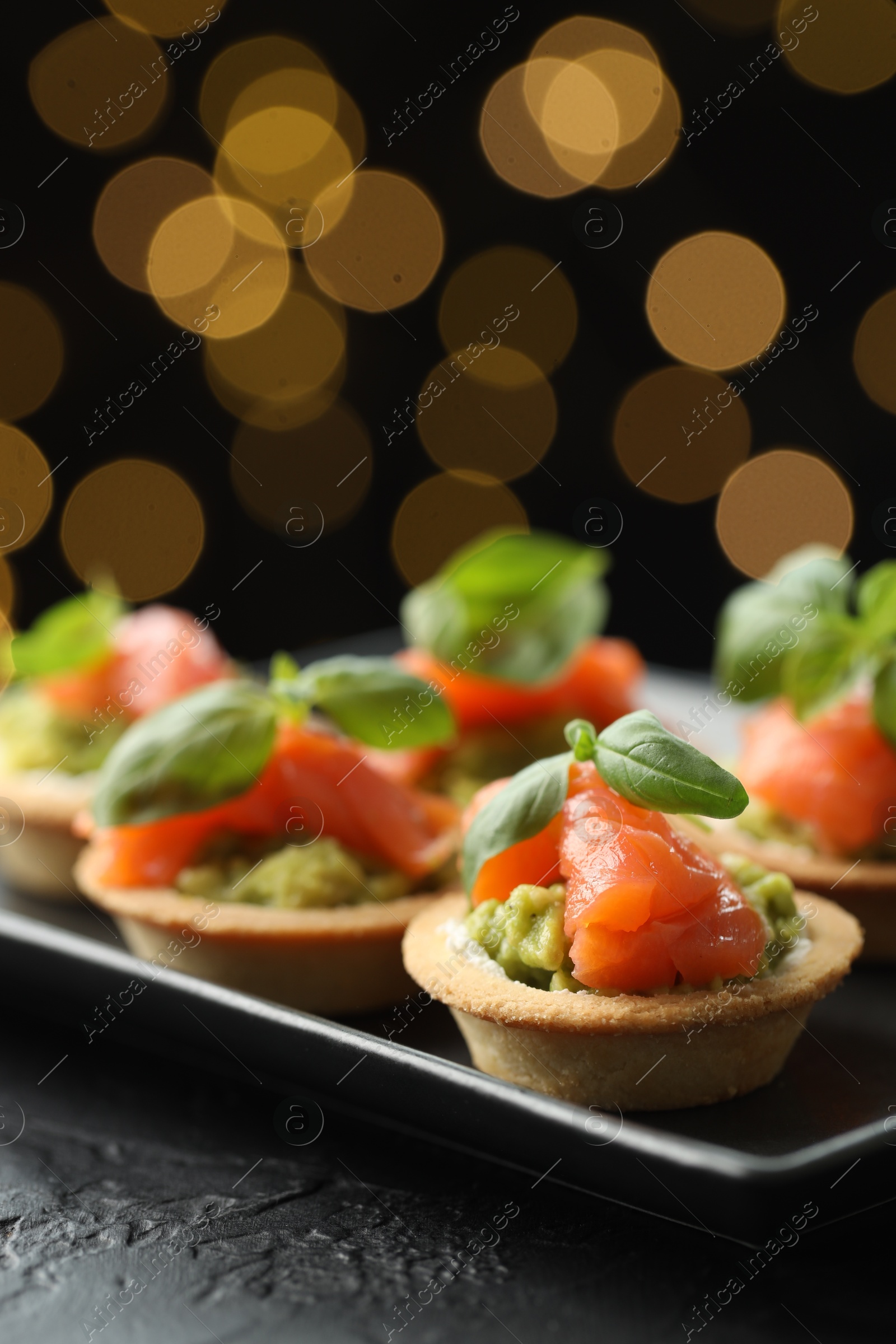 Photo of Tasty canapes on black table against dark background with blurred lights, closeup. Bokeh effect