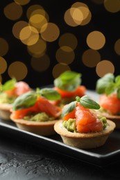 Photo of Tasty canapes on black table against dark background with blurred lights, closeup. Bokeh effect