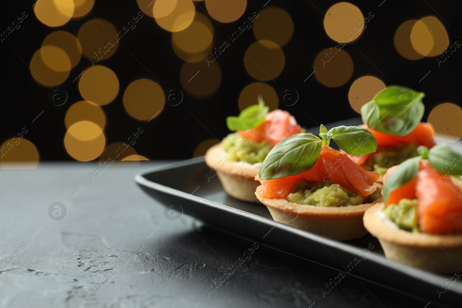 Photo of Tasty canapes on black table against dark background with blurred lights, space for text. Bokeh effect