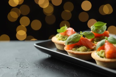 Photo of Tasty canapes on black table against dark background with blurred lights, space for text. Bokeh effect