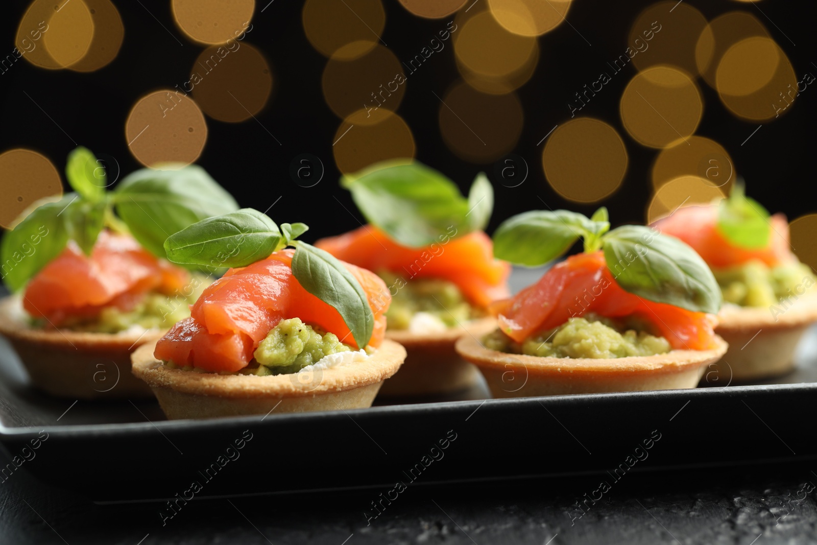 Photo of Tasty canapes on black table against dark background with blurred lights, closeup. Bokeh effect
