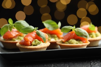 Photo of Tasty canapes on black table against dark background with blurred lights, closeup. Bokeh effect