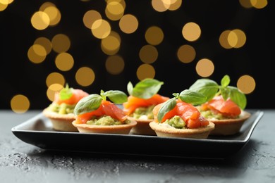 Photo of Tasty canapes on black table against dark background with blurred lights, closeup. Bokeh effect