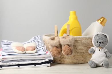 Photo of Bottles of fabric softeners, baby clothes and toy on light wooden table against grey background