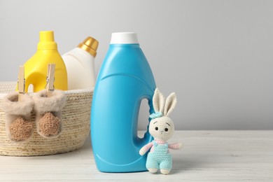 Photo of Bottles of fabric softeners, baby socks and toy on light wooden table against grey background