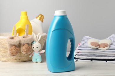 Photo of Bottles of fabric softeners, baby clothes and toy on light wooden table against grey background