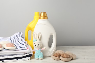Photo of Bottles of fabric softeners, baby clothes and toy on light wooden table against grey background