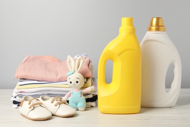 Photo of Bottles of fabric softeners, baby clothes and toy on light wooden table against grey background