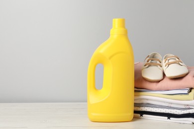 Photo of Bottle of fabric softener, baby clothes and shoes on light wooden table against grey background. Space for text