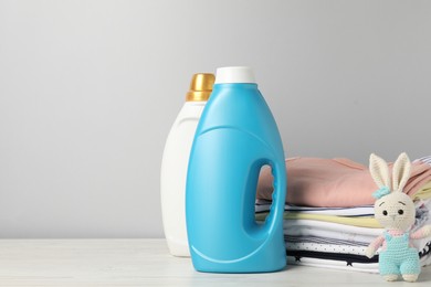 Photo of Bottles of fabric softeners, baby clothes and toy on light wooden table against grey background