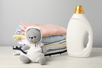 Photo of Bottle of fabric softener, baby clothes and toy on light wooden table against grey background