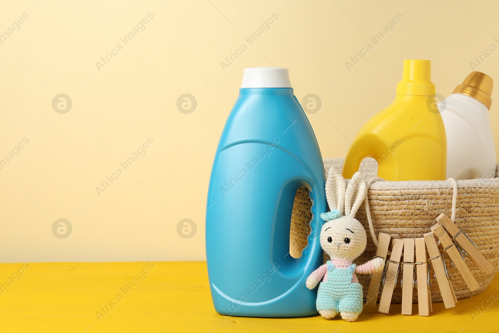 Bottles with fabric softeners, clothespins and toy on yellow wooden table against beige background. Space for text Photo of Bottles with fabric softeners, clothespins and toy on yellow wooden table against beige background. Space for text