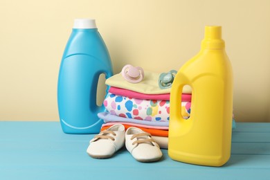 Photo of Bottles with fabric softeners, baby clothes and pacifiers on light blue wooden table against beige background