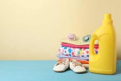 Photo of Bottle with fabric softener, baby clothes and pacifiers on light blue wooden table against beige background. Space for text