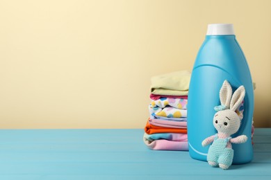 Photo of Bottle with fabric softener, baby clothes and toy on light blue wooden table against beige background. Space for text